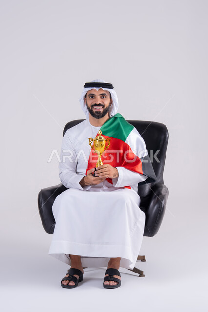 ايماءات وجه تدل على النصر , متابعة المباراة و دعم وتشجيع المنتخب العربي , بورتريه لرجل عربي خليجي اماراتي يرتدي الكندوره والغتره ، يمسك بيده الكأس ويشاهد مباراة للدوري العربي في المنزل, مفهوم الأندية والتشجيع