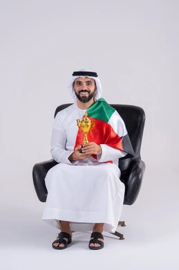 ايماءات وجه تدل على النصر , متابعة المباراة و دعم وتشجيع المنتخب العربي , بورتريه لرجل عربي خليجي اماراتي يرتدي الكندوره والغتره ، يمسك بيده الكأس ويشاهد مباراة للدوري العربي في المنزل, مفهوم الأندية والتشجيع