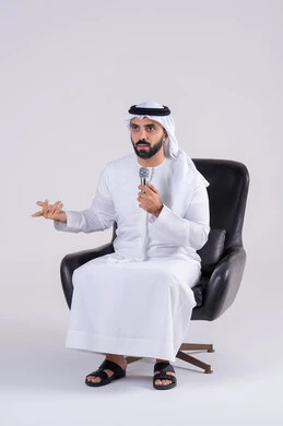 تعابير الاندماج والتفاعل مع الموسيقي اثناء الغناء، ممارسة موهبة الغناء،  تسجيل مقطع صوتي غنائي،بورتريه لرجل عربي خليجي اماراتي يرتدي الكندوره والغتره يمسك بيده المايكروفون ، تقديم العروض الصوتية