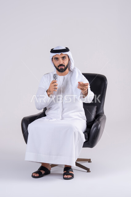 تسجيل مقطع صوتي غنائي، الاشاره باصبع السبابه ،ممارسة موهبة الغناء، بورتريه لرجل عربي خليجي اماراتي يرتدي الكندوره والغتره يمسك بيده المايكروفون ، تعابير الاندماج والتفاعل مع الموسيقي اثناء الغناء، تقديم العروض الصوتية