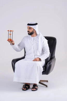 إدراك قيمة اللحظات الثمينة, مفهوم إدارة الأعمال وتنظيم الجدول الزمني, مراقبة توقيت الرمل, بورتريه لرجل عربي خليجي اماراتي يرتدي الكندوره والغتره، يمسك بيده الساعة الرملية الزجاجية (البنكام), النظر بإيماءات التركيز
