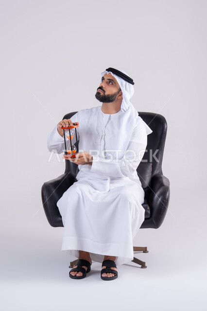 إدراك قيمة اللحظات الثمينة, مفهوم إدارة الأعمال وتنظيم الجدول الزمني, مراقبة توقيت الرمل,  بورتريه لرجل عربي خليجي اماراتي يرتدي الكندوره والغتره، يمسك بيده الساعة الرملية الزجاجية (البنكام), النظر بإيماءات التركيز
