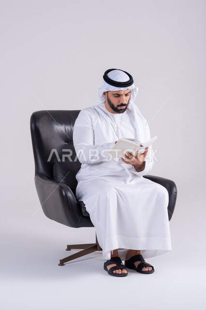 التزود بالعلم والمعرفة،مفهوم العلم والدين والثقافه، قضاء وقت الفراغ بالتثقيف والتعلم،بورتريه لرجل عربي خليجي اماراتي يرتدي الكندوره والغتره يجلس على كرسي، يمارس هواية مطالعة الكتب المفيدة في وقت الفراغ، إيماءات التمعن والتركيز