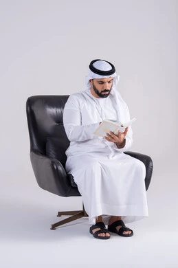 التزود بالعلم والمعرفة،مفهوم العلم والدين والثقافه، قضاء وقت الفراغ بالتثقيف والتعلم،بورتريه لرجل عربي خليجي اماراتي يرتدي الكندوره والغتره يجلس على كرسي، يمارس هواية مطالعة الكتب المفيدة في وقت الفراغ، إيماءات التمعن والتركيز