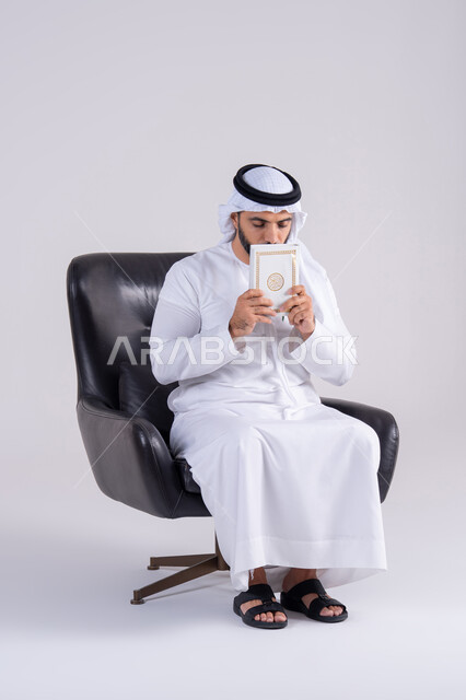 Acquiring knowledge and learning. The concept of knowledge, religion, and culture. Spending free time in education and learning. Portrait of an Emirati Gulf Arab man wearing a kandura and ghutra, sitting on a chair and holding a book. Hobby of reading useful books in free time. Gestures of contemplation and concentration.