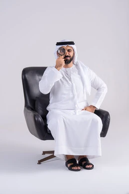 Portrait of an Emirati Gulf Arab man wearing a kandura and ghutra, looking through a magnifying glass with gestures of concentration, examination, exploration, and close-up, scrutinizing with optical tools. This is the concept of image clarification.