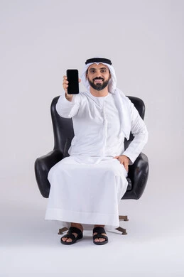 عرض شاشه الهاتف المحمول ،التقاط صور السيلفي ،  الدردشة والتحدث مع الأصدقاء، بورتريه لرجل عربي خليجي اماراتي يرتدي الكندوره والغتره يمسك الجوال بيده، استخدام التقنيات والتكنولوجيا الحديثة بالحياة اليومية