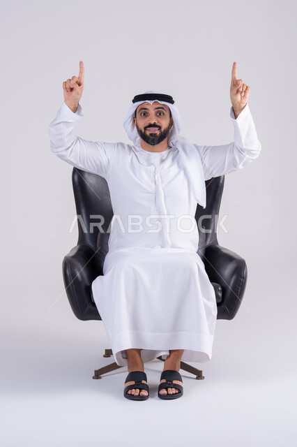 النظر إلى الكاميرا بإيماءات الفرح والسرور، تحديد موقع معين ، تعابير تحدد هذا المكان هنا، بورتريه لرجل عربي خليجي اماراتي يرتدي الكندوره والغتره، يشير بإصبع السبابة لاعلى