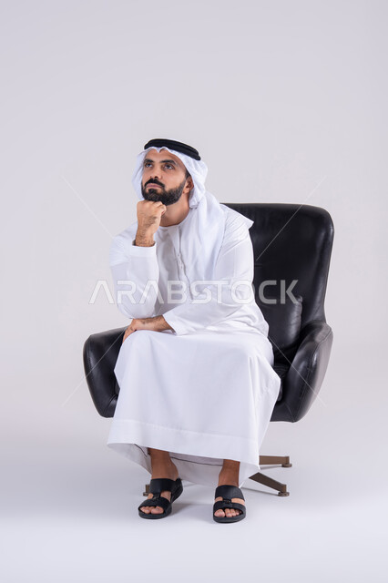 Trying to find a solution to difficult problems, deep thinking and absent-mindedness, anxiety and confusion about making the right decision. Portrait of an Arab Gulf Emirati man wearing a kandura and ghutra, placing his hand under his chin. Expressions and gestures of integration.