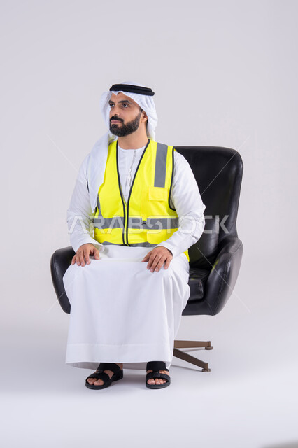 The concept of engineering and architectural construction, working in the engineering sector, expressions of pleasure, happiness and self-confidence, a portrait of an Arab Gulf Emirati man wearing a kandura, ghutra and a protective vest, looking with gestures of pride.