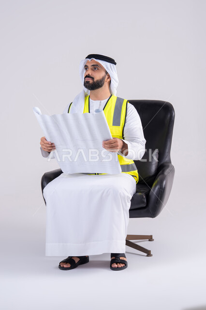 Developing engineering projects in the UAE by its people, supervising and monitoring engineering projects. Portrait of an Emirati Gulf Arab man wearing a protective vest and holding construction plans.