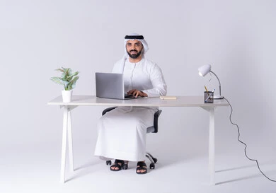 التوظيف في المكاتب والشركات ، التركيز والتفاني والعمل الجاد،استخدم التقنيات الحديثة في الأعمال الإدارية ، بورتريه لرجل عربي خليجي اماراتي يرتدي الكندوره والغتره يجلس على مكتب ويعمل على جهاز الحاسوب المحمول ،دمج التكنولوجيا المتطوره فى الحياه اليوميه