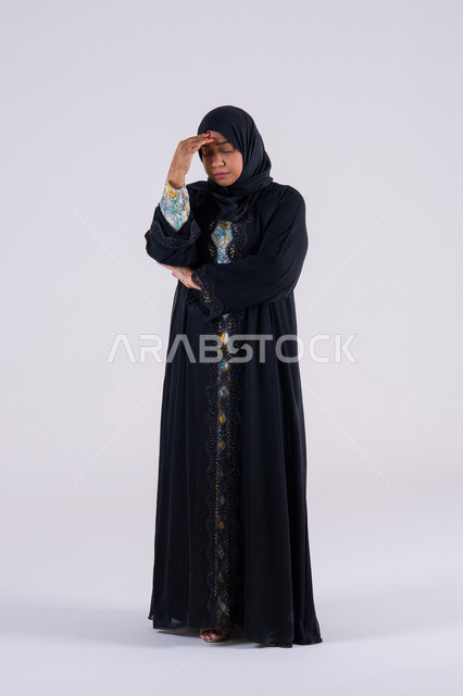 Trying to find a solution to difficult problems, anxiety and confusion in making the right decision, deep thinking and absent-mindedness. Portrait of an Arab Gulf Emirati woman wearing an abaya and hijab, placing her hand under her face. A Saudi woman standing with gestures of confusion.