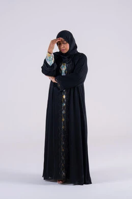 Trying to find a solution to difficult problems, anxiety and confusion in making the right decision, deep thinking and absent-mindedness. Portrait of an Arab Gulf Emirati woman wearing an abaya and hijab, placing her hand under her face. A Saudi woman standing with gestures of confusion.