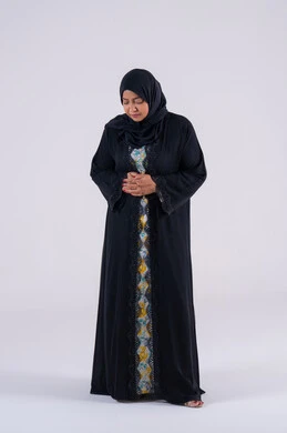 Facial and hand movements indicating distress and discomfort. A Saudi woman feels tired, and needs to rest and receive appropriate treatment. A portrait of an Arab Gulf Emirati woman wearing an abaya and hijab, placing her hands on her stomach with an expression of pain, feeling sick, and having abdominal pain.