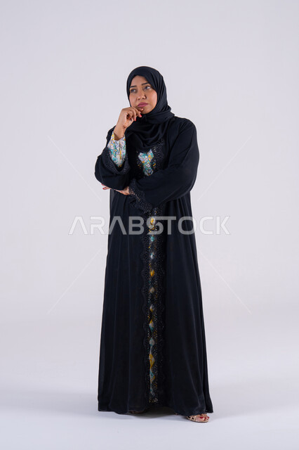 القلق والحيرة في اتخاذ القرار الصحيح، محاولة إيجاد حل للمشكلات الصعبة، التفكير بعمق وشرود الذهن، بورتريه لامراه عربيه خليجيه اماراتيه ترتدي العباءه والحجاب تضع يدها أسفل ذقنها ، سيده سعوديه تقف بإيماءات الاندماج
