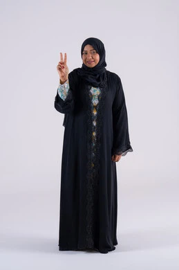 Success and goal achievement: A Saudi woman standing with an expression of joy and happiness. A portrait of a smiling, veiled, Emirati Gulf Arab woman wearing a black abaya, looking at the camera with facial and hand gestures indicating victory and triumph.
