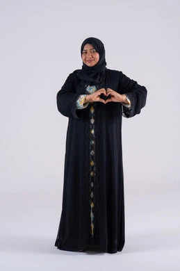 سيده سعوديه تقف بايماءات يدين على شكل قلب، اظهار مشاعر الحب والشغف، مفهوم المحبة والمودة، بورتريه لامرأه عربيه خليجيه اماراتيه محجبة ترتدي عباءة سوداء تنظر إلى الكاميرا بتعابير السرور والسعادة