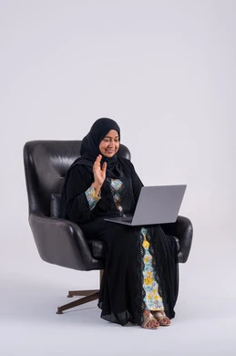 Making video calls, completing work tasks remotely, using modern technologies in administrative work, portrait of a Saudi Arabian Gulf woman wearing an abaya and hijab sitting on a chair and working on a laptop, integrating advanced technology into daily life. Making video calls, completing work tasks remotely, using modern technologies in administrative work, portrait of a Saudi Arabian Gulf woman wearing an abaya and hijab sitting on a chair and working on a laptop, integrating advanced technology into daily life.
