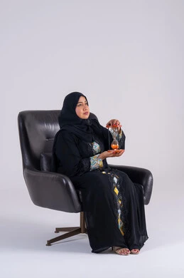 تعابير الاندماج والتفاعل، النظر بإيماءات الانتظار ،سيده سعوديه تقوم بمراقبة توقيت الرمل, إدراك قيمة اللحظات الثمينة,  مفهوم إدارة الأعمال وتنظيم الجدول الزمني,بورتريه لامراه عربيه خليجيه اماراتيه ترتدي العباءه والحجاب تمسك بيدها الساعة الرملية الزجاجية (البنكام)