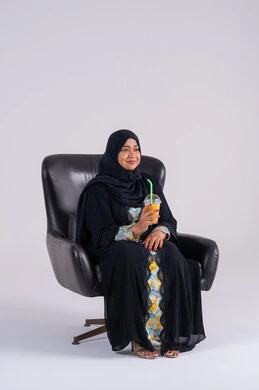 Watching TV shows, having a good time at home, gestures of surprise and amazement, home entertainment activities, a Saudi woman drinking cold drinks, a portrait of an Arab Gulf Emirati woman wearing an abaya and hijab, enjoying watching movies and TV series.