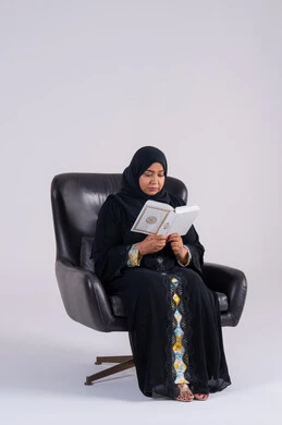 Gaining knowledge and science, the concept of literacy, spending free time educating and learning, a portrait of an Arab Gulf Emirati woman wearing an abaya and hijab sitting on a chair, practicing her hobby of reading useful books in her free time, a Saudi woman reading with gestures of contemplation and concentration.