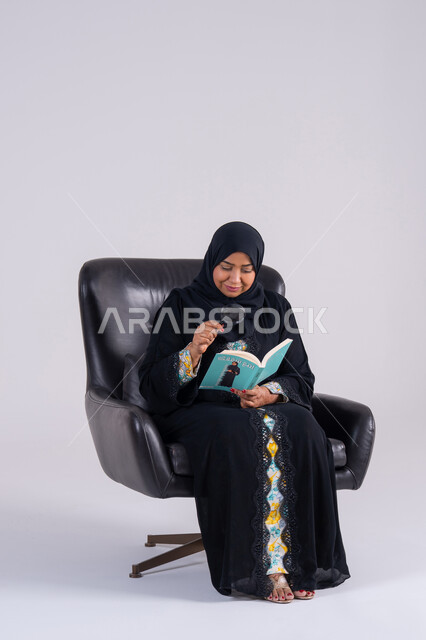 الفحص والاستكشاف والرؤية عن قرب،مفهوم توضيح الصورة، سيده سعوديه تقوم بالتدقيق باستخدام الأدوات البصرية،  بورتريه لامرأة عربية خليجية اماراتيه ترتدي الحجاب والعباءة تحمل كتاب تنظر من خلال العدسة المكبرة اليه بإيماءات التركيز