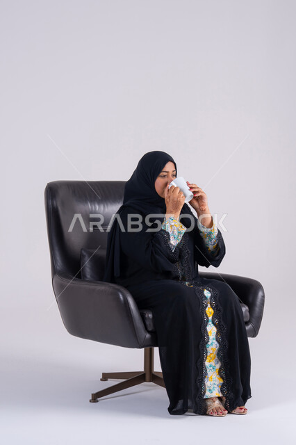 الاستمتاع والاحساس بالدفء ، الحيوية والنشاط عند شرب الكافيين، بورتريه  لامراه عربيه خليجيه اماراتيه ترتدي العباءه والحجاب تحمل بيدها كوب القهوة بتعابير السرور، سيده سعوديه تقوم باحتساء المشروبات الساخنة