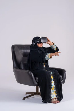 المتعة والتسلية بالمشاهدة عبر نظارة الواقع الافتراضي,  بورتريه لامراه عربيه خليجيه اماراتيه ترتدي العباءه والحجاب تضع نظارات ثلاثية الأبعاد، تنظر بتعابير الاندماج , سيده سعوديه تشير باصبع السبابه الى شئ ما
