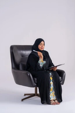 إدارة الأعمال وتنظيمها، سيده سعوديه تستخدم الاوراق البيضاء الفارغة في العمل، تدوين وتسجيل الملاحظات والمعلومات على الورق, بورتريه لامراه عربيه خليجيه اماراتيه  ترتدي العباءه والحجاب تجلس على كرسي ، وتقوم بكتابة المهام والأهداف اليومية