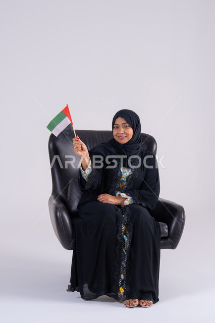 هوية اليوم الوطني الاماراتي 2 ديسمبر، رفع العلم بايماءات الاعتزاز والثقة، احياء ذكرى استقلال الإمارات 1971، الحب والانتماء للوطن، تعابير السرور والفخر والسعاده،  بورتريه لسيده عربية خليجية اماراتيه محجبة تمسك بيدها علم الإمارات