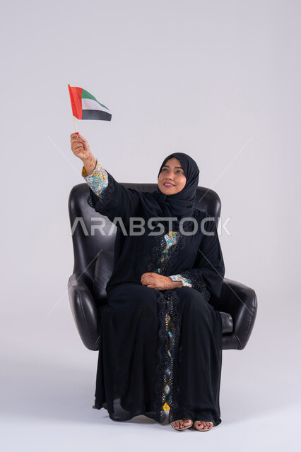 Raising the flag with gestures of pride and confidence, the identity of the UAE National Day, December 2, commemorating the UAE's independence in 1971, love and belonging to the homeland, expressions of joy, pride and happiness, a portrait of a veiled Emirati Gulf Arab woman holding the UAE flag in her hand