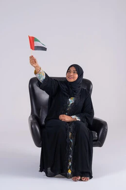رفع العلم بايماءات الاعتزاز والثقة، هوية اليوم الوطني الاماراتي 2 ديسمبر، احياء ذكرى استقلال الإمارات 1971، الحب والانتماء للوطن، تعابير السرور والفخر والسعاده،  بورتريه لسيده عربية خليجية اماراتيه محجبة تمسك بيدها علم الإمارات