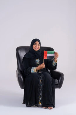 هوية اليوم الوطني الاماراتي 2 ديسمبر، احياء ذكرى استقلال الإمارات 1971، الحب والانتماء للوطن، تعابير السرور والفخر والسعاده، النظر بايماءات الاعتزاز والثقة، بورتريه لسيده عربية خليجية اماراتيه محجبة تمسك بيدها علم الإمارات