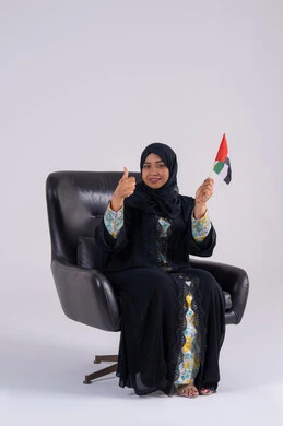 النظر الى الكاميرا بايماءات الاعتزاز والثقة، بورتريه لسيده عربية خليجية اماراتيه محجبة تمسك بيدها علم الإمارات ، هوية اليوم الوطني الاماراتي 2 ديسمبر، احياء ذكرى استقلال الإمارات 1971، الحب والانتماء للوطن