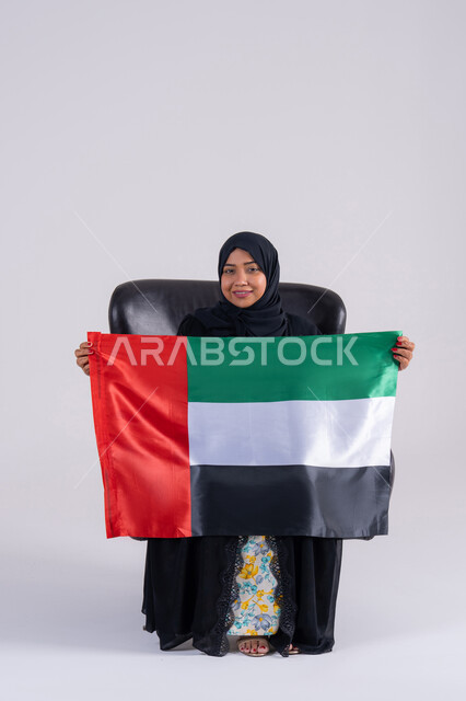 النظر الى الكاميرا بايماءات الاعتزاز والثقة، احياء ذكرى استقلال الإمارات 1971، الحب والانتماء للوطن،بورتريه لسيده عربية خليجية اماراتيه محجبة تحمل علم الإمارات ، هوية اليوم الوطني الاماراتي 2 ديسمبر