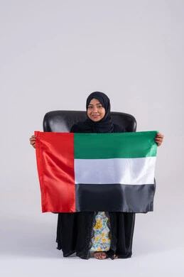 Looking at the camera with gestures of pride and confidence, commemorating the UAE's independence in 1971, love and belonging to the homeland, a portrait of a veiled Emirati Gulf Arab woman holding the UAE flag, the identity of the UAE National Day, December 2