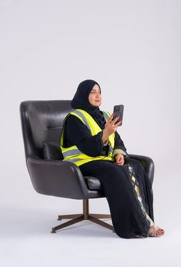 استخدام التقنيات الحديثة،سيده اماراتيه تتابع العمل والمهام، الاشراف والرقابة على المشاريع الهندسية، بورتريه لامراه عربيه خليجيه سعوديه ترتدي العباءه والحجاب تجلس على كرسي وتحمل بيدها الهاتف المحمول