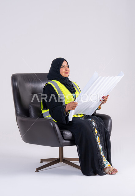 A Saudi woman is developing engineering projects in the Kingdom of Saudi Arabia at the hands of her sons, supervising and monitoring engineering projects, a portrait of a veiled Gulf Arab Emirati engineer wearing a protective jacket and holding construction plans in her hand