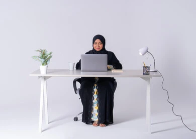 امراه عربيه خليجيه سعوديه ترتدي العباءه والحجاب تجلس على مكتب وتعمل على جهاز الحاسب المحمول ، احتساء المشروبات الساخنه،استخدم التقنيات الحديثة في الأعمال الإدارية ،  سيده اماراتيه تقوم بالتركيز والتفاني والعمل الجاد، التوظيف في المكاتب والشركات ،دمج التكنولوجيا المتطوره فى الحياه اليوميه