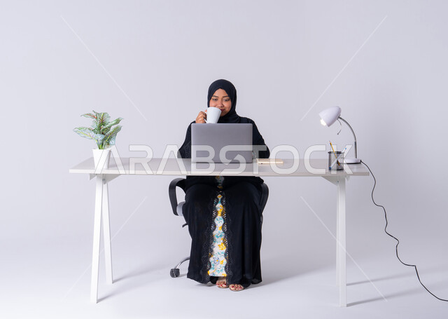 استخدم التقنيات الحديثة في الأعمال الإدارية ، امراه عربيه خليجيه سعوديه ترتدي العباءه والحجاب تجلس على مكتب وتعمل على جهاز الحاسب المحمول ، احتساء المشروبات الساخنه، سيده اماراتيه تقوم بالتركيز والتفاني والعمل الجاد، التوظيف في المكاتب والشركات ،دمج التكنولوجيا المتطوره فى الحياه اليوميه