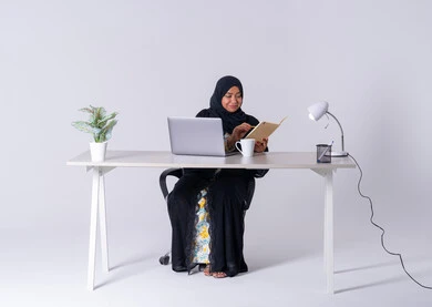 بورتريه لامراه عربيه خليجيه سعوديه ترتدي العباءه والحجاب تجلس على مكتب ،تعمل على جهاز الحاسوب المحمول ، تدوين تقارير العمل, احتساء المشروبات الساخنه، كتابة مهام واهداف العمل ،سيده اماراتيه تقوم باداره الأعمال عن بعد وتنظيمها، استخدم التقنيات الحديثة في الأعمال الإدارية
