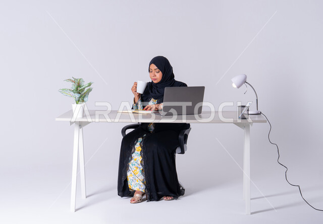استخدم التقنيات الحديثة في الأعمال الإدارية ، دمج التكنولوجيا المتطوره فى الحياه اليوميه ، التركيز والتفاني والعمل الجاد،التوظيف في المكاتب والشركات ، امراه عربيه خليجيه سعوديه ترتدي العباءه والحجاب تجلس على مكتب وتعمل على جهاز الحاسب المحمول ، سيده اماراتيه تقوم باحتساء المشروبات الساخنه