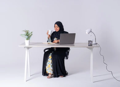 دمج التكنولوجيا المتطوره فى الحياه اليوميه ، التركيز والتفاني والعمل الجاد،التوظيف في المكاتب والشركات ،استخدم التقنيات الحديثة في الأعمال الإدارية ،  امراه عربيه خليجيه سعوديه ترتدي العباءه والحجاب تجلس على مكتب وتعمل على جهاز الحاسب المحمول ، سيده اماراتيه تقوم باحتساء المشروبات الساخنه