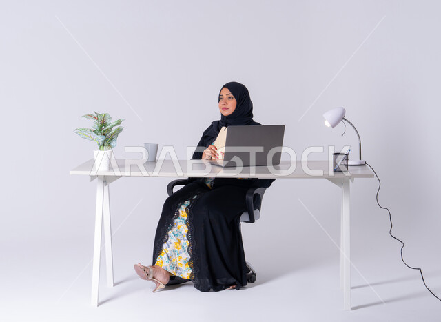سيده اماراتيه تقوم باداره الأعمال عن بعد وتنظيمها، كتابة مهام واهداف العمل ، احتساء المشروبات الساخنه،بورتريه لامراه عربيه خليجيه سعوديه ترتدي العباءه والحجاب تجلس على مكتب ،تعمل على جهاز الحاسوب المحمول ، تدوين تقارير العمل,استخدم التقنيات الحديثة في الأعمال الإدارية