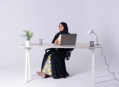 Emirati woman managing and organizing business remotely, writing down work tasks and goals, drinking hot drinks, portrait of a Saudi Arabian Gulf woman wearing an abaya and hijab sitting at a desk, working on a laptop, writing work reports, using modern technologies in administrative work