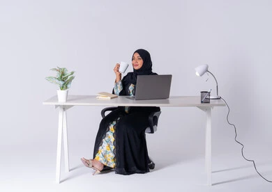 التوظيف في المكاتب والشركات ، التركيز والتفاني والعمل الجاد،استخدم التقنيات الحديثة في الأعمال الإدارية ،  بورتريه لامراه عربيه خليجيه سعوديه ترتدي العباءه والحجاب تجلس على مكتب وتعمل على جهاز الحاسب المحمول ،دمج التكنولوجيا المتطوره فى الحياه اليوميه ، سيده اماراتيه تقوم باحتساء المشروبات الساخنه