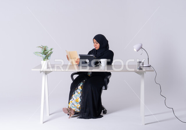 استخدم التقنيات الحديثة في الأعمال الإدارية ، سيده اماراتيه تقوم بإدارة الأعمال عن بعد وتنظيمها، تدوين وتسجيل الملاحظات والمعلومات على الورق, بورتريه لامراه عربيه خليجيه سعوديه ترتدي العباءه والحجاب تجلس على مكتب ،تعمل على جهاز التابلت ،كتابة مهام واهداف العمل ، احتساء المشروبات الساخنه