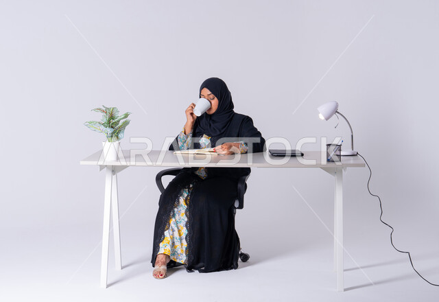 احتساء المشروبات الساخنه، سيده اماراتيه تقوم بإدارة الأعمال وتنظيمها، استخدام الاوراق البيضاء الفارغة في العمل، تدوين وتسجيل الملاحظات والمعلومات على الورق, بورتريه لامراه عربيه خليجيه سعوديه ترتدي العباءه والحجاب تجلس على مكتب ، وتقوم بكتابة المهام والأهداف اليومية