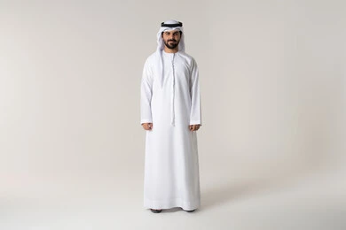 The concept of elegance, masculinity, and strength, entertainment by listening to audio clips through headphones, following music and entertainment with headphones, wearing audio headsets, a portrait of an Emirati Gulf Arab man wearing the Emirati kandura listening to songs with gestures of joy and happiness, white background.